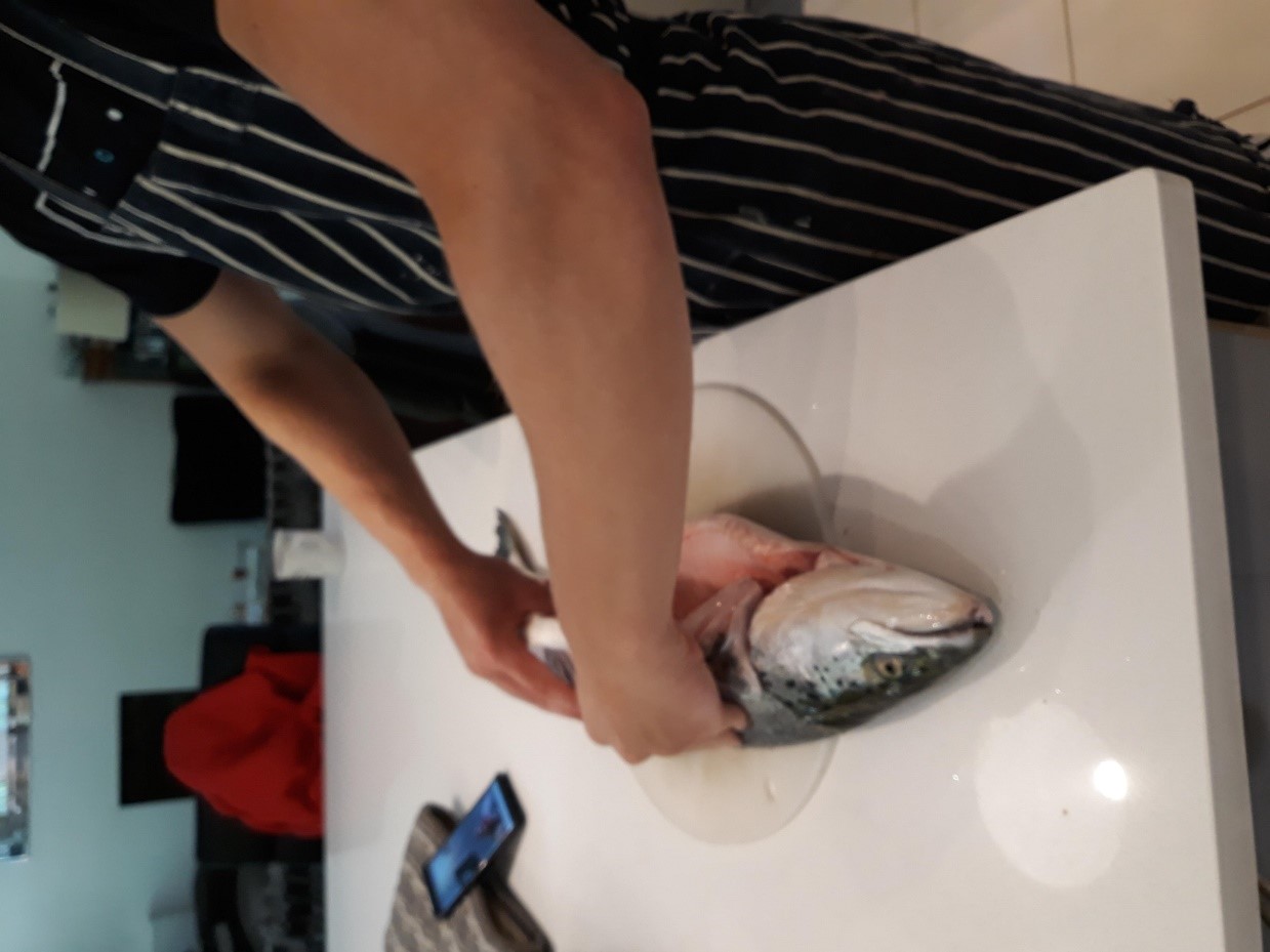 A person standing in a kitchen about to prepare fish.

